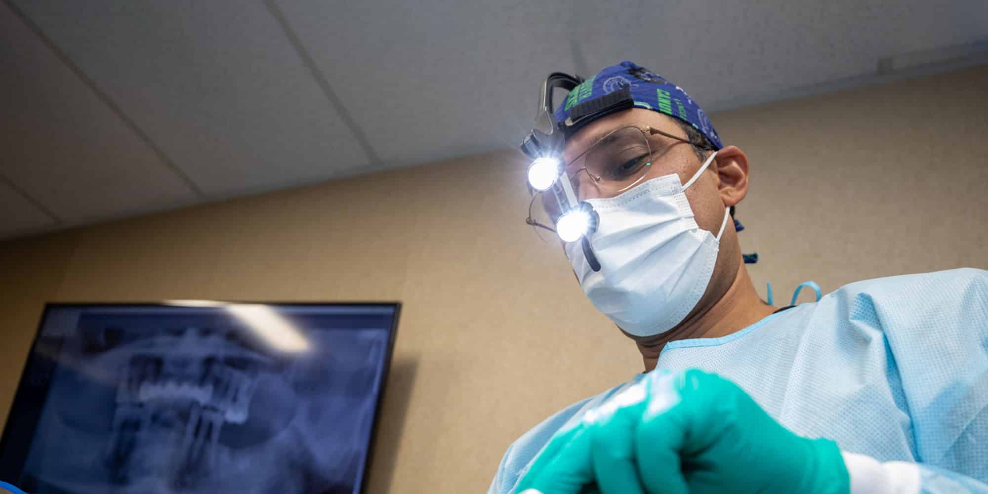 surgical gear on as dr bhullar performs dental procedure